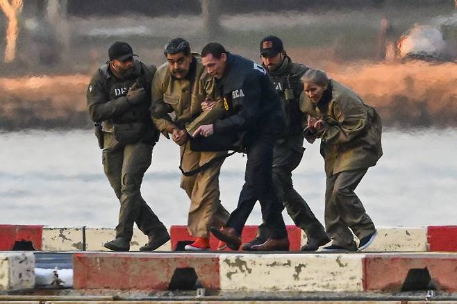 법원으로 향하는 마두로 부부 니콜라스 마두로 베네수엘라 대통령과 부인 실리아 플로레스가 5일(현지시간) 헬기 편으로 미국 뉴욕 월스트리트 헬기장에 도착한 뒤 마약단속국 직원들에게 붙들린 채 뉴욕 남부연방법원으로 이동하고 있다. EPA연합뉴스