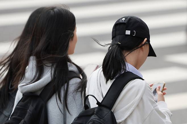 Students check their phones near a middle school in downtown Seoul after school on Nov. 4, 2024. [YONHAP]