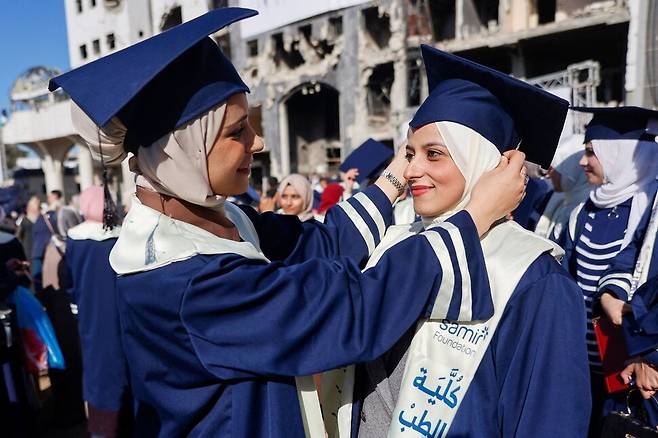 2026년 1월3일 팔레스타인 땅 가자지구 북부 가자시티의 알시파병원 앞마당에서 열린 의대생 합동 졸업식에서 한 학생이 동료의 학사모를 바로잡아주고 있다. AFP 연합뉴스