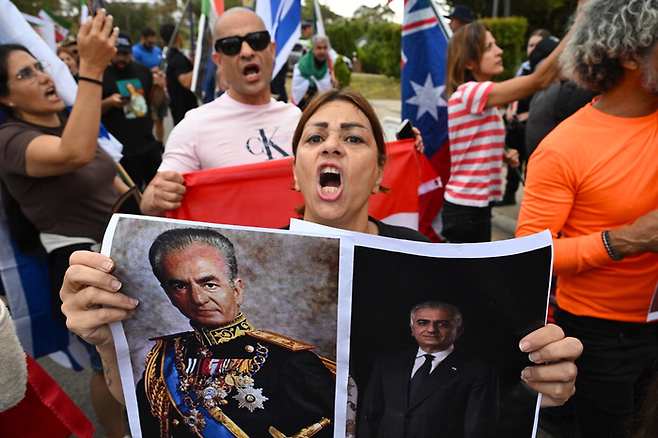 15일(현지시간) 호주 캔버라 주재 이란 대사관 인근에서 열린 이란 반정부 시위에서 한 참여자가 이란 팔레비 왕조 마지막 샤(국왕)인 무함마드 리자 팔레비(왼쪽)와 미국에 망명 중인 리자 팔레비 전 이란 왕세자의 사진을 들고 구호를 외치고 있다. [EPA = 연합뉴스]
