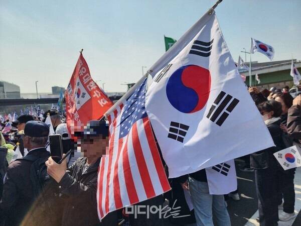 ▲지난해 4월 윤석열 대통령 탄핵심판 선고를 앞둔 가운데 열린 한남동 인근 탄핵반대 집회에서 참가자가 성조기와 태극기를 들고 있다. 사진=윤수현 기자