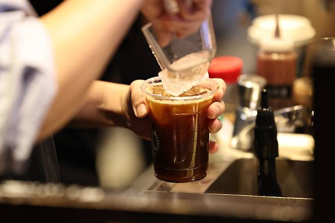 A cafe employee puts ice into a plastic cup full of coffee at a cafe in Seoul on Dec. 18, 2025. [YONHAP]