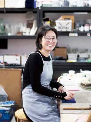 유리 조형가 정수경이 작업대에 앉아 밝게 웃어 보인다.