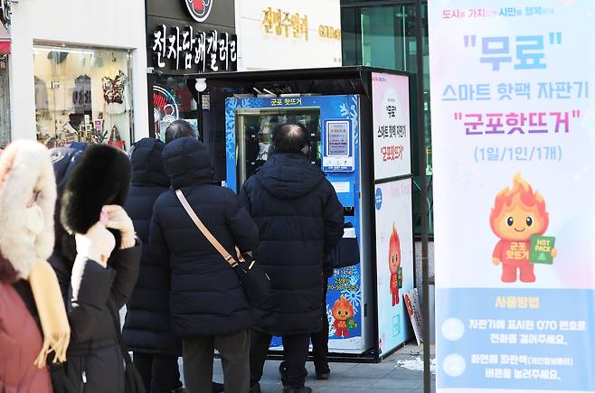 Residents line up to receive free hand warmers from a “Gunpo Hot-Teogeo” smart vending machine on Sanbon Rodeo Street in Gunpo, south of Seoul, on Jan. 21, as a severe cold wave grips the region. [YONHAP]