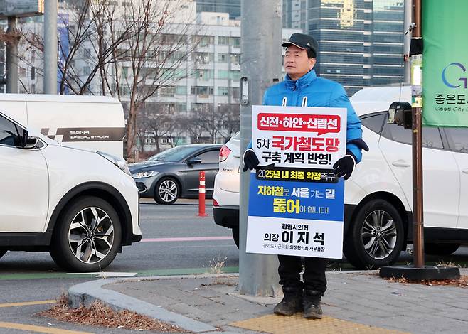 이지석 광명시의회 의장이 거리에서 시민들에게 신천·하안·신림선의 국가철도망 구축 계획 반영을 호소하는 푯말을 들고 서 있다. 사진=광명시의회