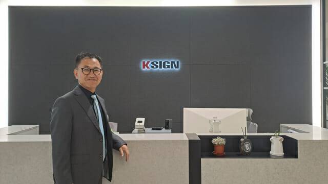 구자동 케이사인 대표가 회사 로고를 배경으로 포즈를 취했다. 올해 케이사인은 PQC와 AI보안에 주력한다.