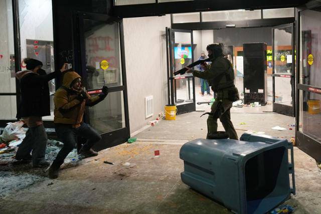 26일 미국 미네소타주 미니애폴리스의 한 호텔 앞에서 연방 요원이 이민세관단속국(ICE) 반대 시위대를 향해 총을 겨누자 시위대가 휴대폰으로 그를 촬영하고 있다. 미니애폴리스=AP 연합뉴스