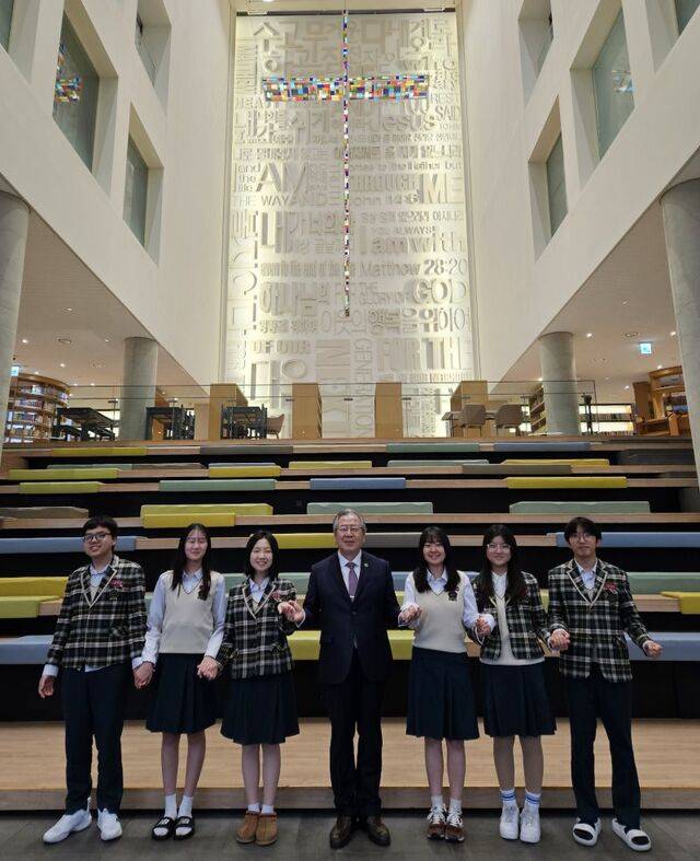 새로남기독학교 이사장인 오정호 새로남교회 목사와 새로남기독학교 학생들이 대전의 학교 로비에서 손을 맞잡고 있다.