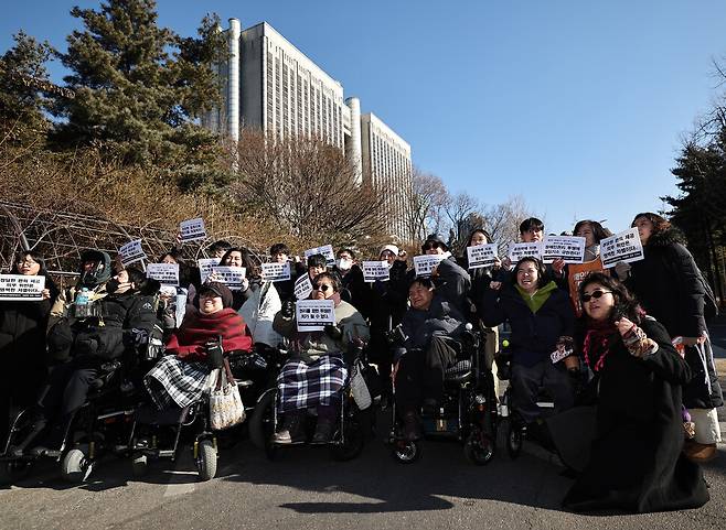 장애인 활동가 문애린(앞줄 오른쪽 둘째)씨와 비장애 활동가 한명희(앞줄 오른쪽 끝)씨가 2026년 1월29일 서울 서초구 서울중앙지방법원 들머리에서 열린 ‘장애인 권리 확보를 위한 투쟁에 대한 무죄판결 촉구 및 장애인 이동권 침해 및 공권력 남용에 대한 차별구제 청구소송 기자회견’을 마친 뒤 재판정에 들어가기에 앞서 참석자들과 기념사진을 찍고 있다.