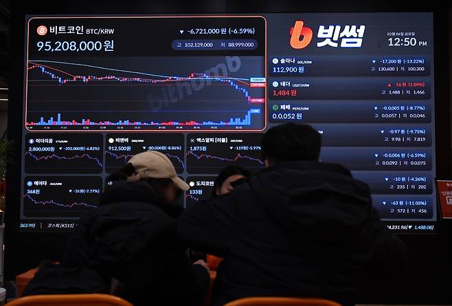 6일 서울 강남구 빗썸 라운지에 설치된 암호화폐 시세 현황판 앞에서 방문객들이 계좌 개설 상담을 받고 있다. /뉴스1