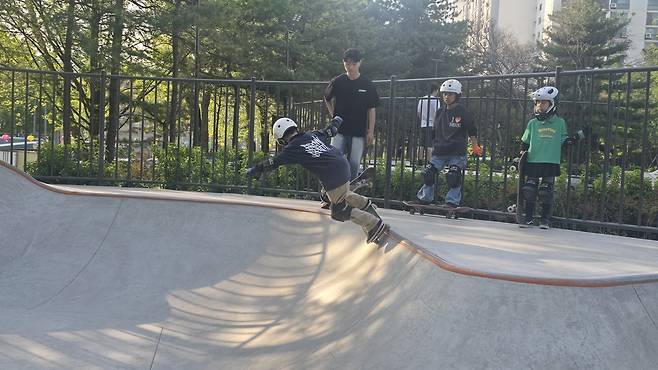 스케이트보드를 타는 사람이 넘어지는 모습이고, 뒤에는 다른 사람들이 서 있다. 노원 엑스탑에서 스케이트보드 강습을 받는 모습이다.