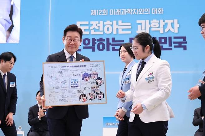 미래 과학자들의 다짐 품은 대통령 - 이재명 대통령이 5일 청와대 영빈관에서 열린 ‘제12회 미래과학자와의 대화’에서 국제과학올림피아드 한국대표단으로부터 각자의 다짐이 적힌 액자를 선물받은 뒤 이를 들어보이고 있다. 뉴스1