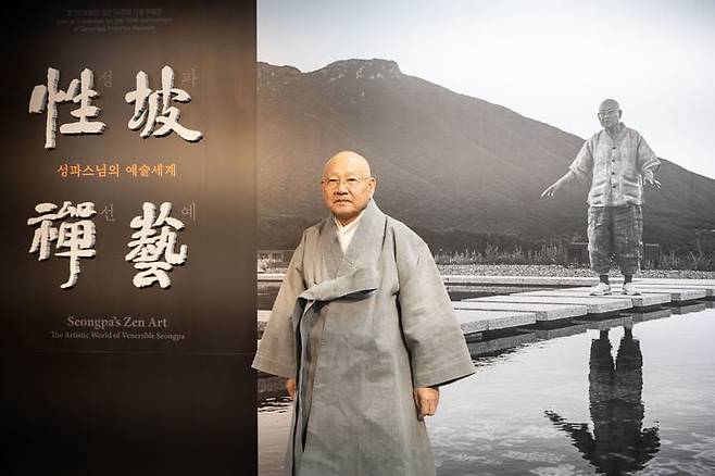 성파 스님이 전시장 입구에서 기념 촬영했다. 뒤의 사진은 통도사 서운암에서 촬영한 모습. /뉴시스