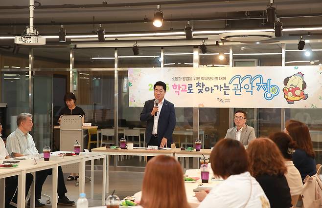 실내에서 박준희 관악구청장이 마이크를 들고 이야기하고 있고, 테이블을 중심으로 사람들이 둘러앉아 있는 사진이다. 배경에는 ‘학교로 찾아가는 관악청’이라고 적힌 배너가 걸려 있다.