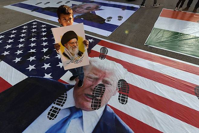 지난 15일 파키스탄 카라치에서 한 어린이가 미국과 이스라엘의 이란 압박에 항의해 아야톨라 알리 하메네이 이란 최고 지도자 그림을 들고 도널드 트럼프 미국 대통령과 미국 국기, 이스라엘 국기 등을 밟는 시위를 벌이고 있다. EPA=연합뉴스