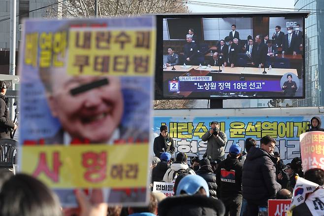 지난 19일 12·3 비상계엄과 관련해 내란 중요임무종사 혐의로 기소된 노상원 전 정보사령관이 1심에서 징역 18년을 선고받았다. 사진은 이날 서울중앙지법 인근 집회 현장에서 시민들이 재판 생중계 영상을 보고 있는 모습이다. ⓒ연합뉴스