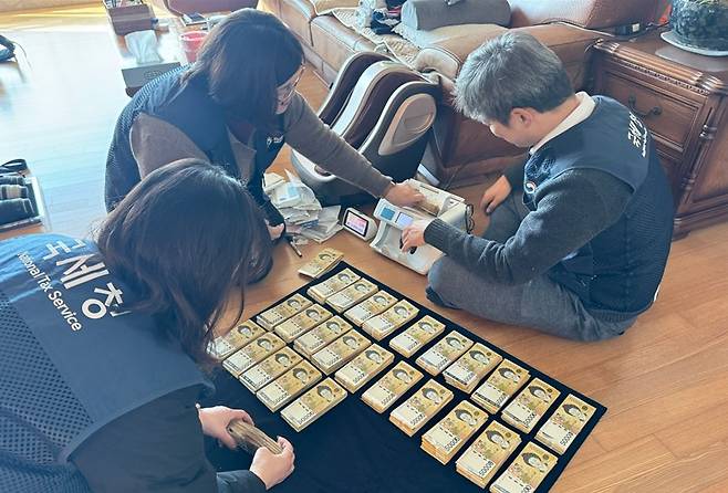 국세청 특별기동반 직원들이 A 씨의 자택 화장실 세면대 수납장에서 5만 원권 현금다발이 담긴 김치통을 발견한 뒤 정확한 금액을 계수하는 모습. 국세청 제공.