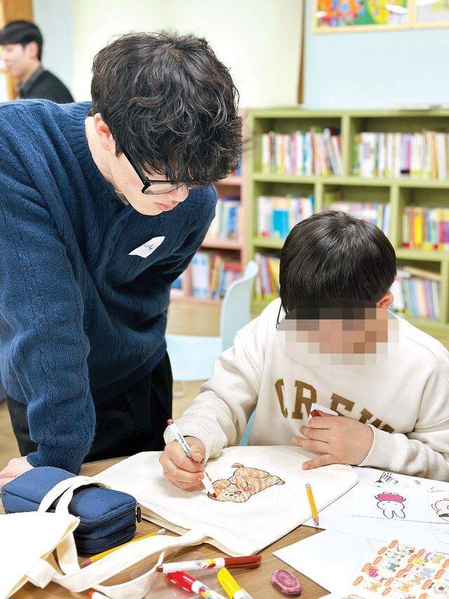 ‘우리들의크리스천커뮤니티(우크)’ 소속 청년 봉사자가 지난달 경기도 화성 신명아이마루보육원에서 에코백에 그림 그리는 아이를 지켜보며 조언하고 있다. 우크 제공