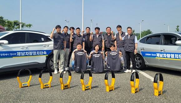 경기도 고양시 체납차량 영치팀 직원들이 단속 차량 앞에서 휠 잠금장치를 나란히 세워둔 채 악성 체납 근절을 다짐하며 주먹을 불끈 쥐고 있다. [사진=고양시]