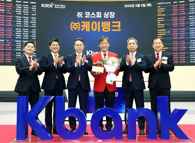 K bank CEO Choi Woo-hyung (in red) poses for photographs at the listing ceremony at the Korea Exchange in Seoul on Thursday. (Korea Exchange)