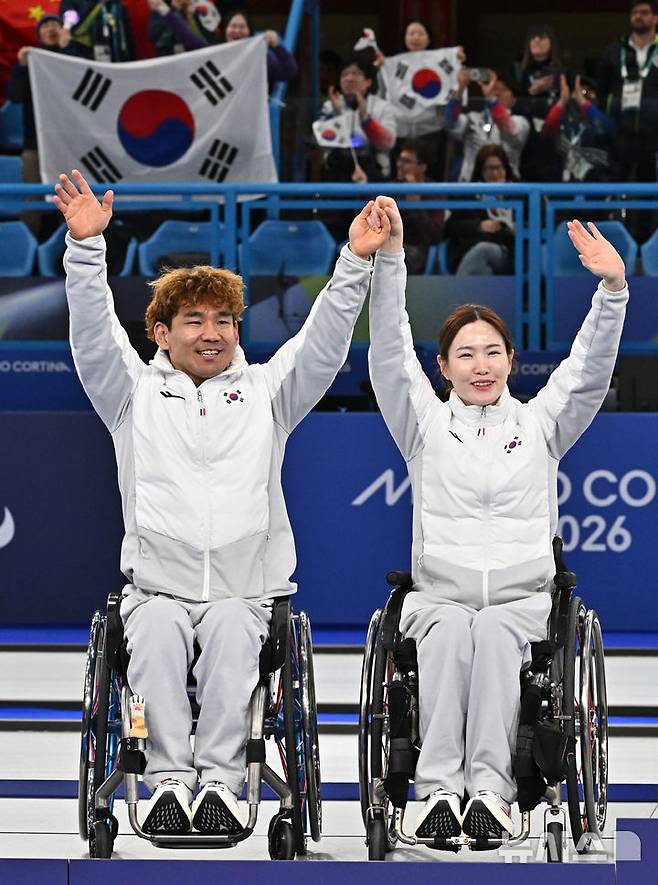 [코르티나담페초=뉴시스] 사진공동취재단 = 휠체어컬링 백혜진(오른쪽)과 이용석이 11일(현지 시간) 이탈리아 코르티나담페초 컬링 올림픽 스타디움에서 열린  2026 밀라노 코르티나 패럴림픽 휠체어컬링 믹스더블에서 은메달을 차지한 뒤 환호하는 관중들에게 인사를 하고 있다. 2026.03.12. photo@newsis.com