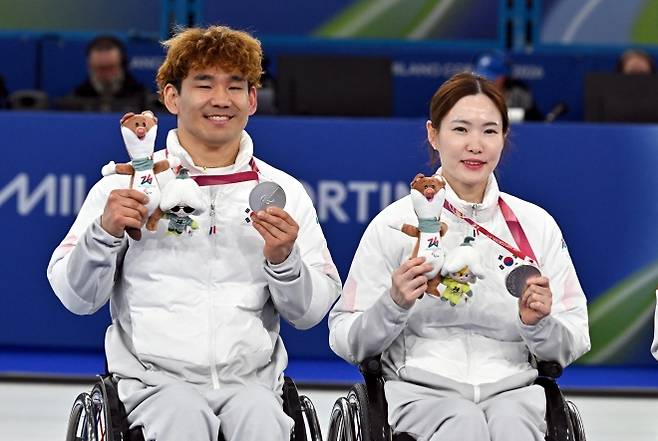 휠체어컬링 백혜진(오른쪽)-이용석이 12일(한국시간) 이탈리아 코르티나담페초 컬링 올림픽 스타디움에서 열린  2026 밀라노 코르티나 패럴림픽 휠체어컬링 믹스더블 시상식에서 은메달을 들어보이며 밝게 웃고 있다. 사진공동취재단