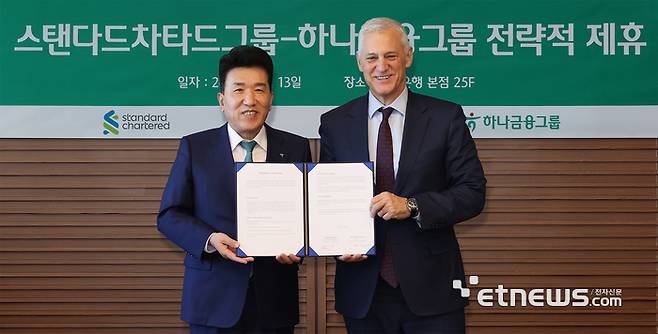 하나금융그룹은 지난 13일 서울 중구 하나은행 본점에서 영국의 글로벌 금융그룹 스탠다드차타드와 글로벌 비즈니스 및 디지털 자산 협력을 위한 업무협약을 체결했다. 협약식에 참석한 함영주 하나금융그룹 회장(왼쪽)이 빌 윈터스 스탠다드차타드그룹 회장과 협약서를 들고 기념 촬영하고 있다. [사진= 하나금융 제공]