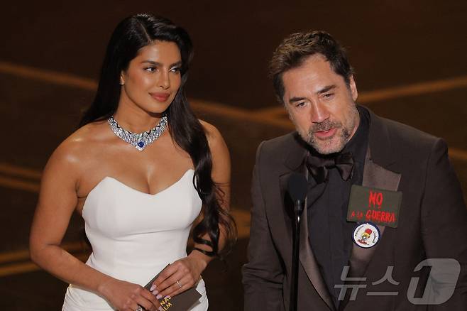 15일(현지시간) 미국 캘리포니아주 로스앤젤레스(LA) 할리우드에서 열린 제98회 아카데미 시상식에서 배우 하비에르 바르뎀(오른쪽)이 '전쟁을 멈춰라'(NO A LA GUERRA)라는 스페인어 문구를 가슴에 착용하고 배우 프리양카 초프라와 함께 무대에 올라 발언하고 있다. 2026.03.15. ⓒ 로이터=뉴스1