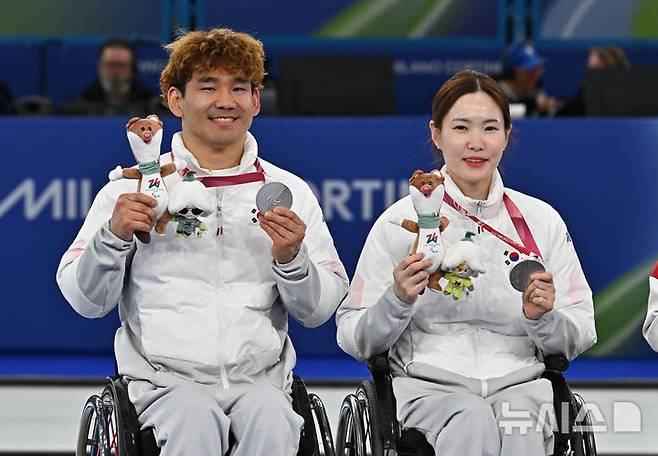 [코르티나담페초=뉴시스] 사진공동취재단 = 휠체어컬링 백혜진(오른쪽)과 이용석이 11일(현지 시간) 이탈리아 코르티나담페초 컬링 올림픽 스타디움에서 열린  2026 밀라노 코르티나 패럴림픽 휠체어컬링 믹스더블에서 은메달을 차지한 뒤 메달을 들어보이고 있다. 2026.03.12. photo@newsis.com