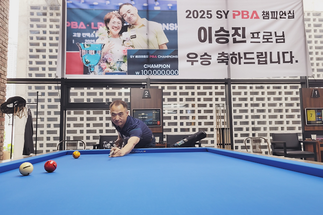 55세에 프로당구에서 첫 우승한 이승진 프로가 지난 15일 대구 수성구의 한 당구장에서 큐대를 잡고 포즈를 취하고 있다. 그의 뒤편엔 아내와 함께 찍은 우승 기념 사진이 걸려 있다. 이효설기자