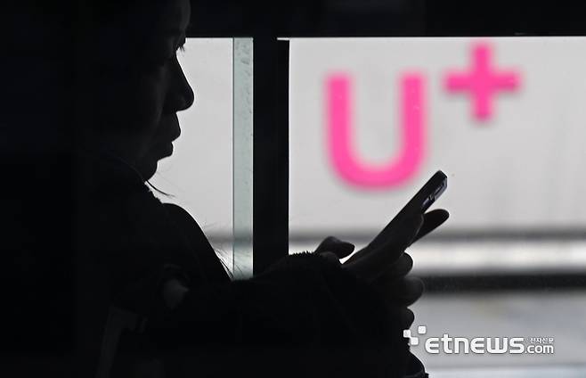 LG유플러스가 사용자의 전화번호가 반영된 가입자식별번호(IMSI) 체계를 장기간 유지한 것으로 드러났다. IMSI는 이동통신 가입자 식별을 위해 유심에 부여되는 고유번호로, LG유플러스는 보안 취약점 해소를 위해 전 고객 대상으로 유심 교체와 재설정을 추진한다. 17일 서울 시내버스에서 스마트폰을 이용하는 시민 너머로 LG유플러스 매장이 보인다.  이동근기자 foto@etnews.com
