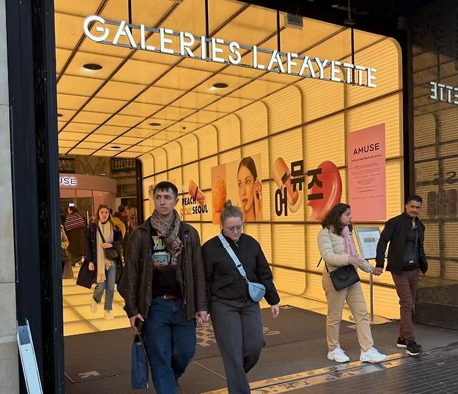 19일(현지시간) 프랑스 파리의 갤러리 라파예트 샹젤리제점에 입구에 K뷰터 브랜드 '어뮤즈'' 한글 대형 홍보물을 바탕으로 현지인들이 드나들고 있다./원선우 특파원