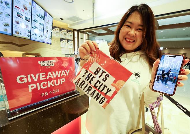 방탄소년단(BTS)의 서울 광화문광장 컴백 공연을 하루 앞둔 20일 인천공항 제1여객터미널 컬리너리스퀘어 바이 아워홈 매장에서 한국을 찾은 BTS 해외팬이 ‘BTS THE CITY Welcome&Farewell’ 세트를 구입하고 받은 스카프 굿즈를 들고 기뻐하고 있다. 뉴시스