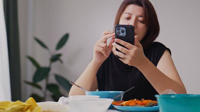 스마트폰을 보며 식사하는 여성의 모습. 음식 콘텐츠 시청이 식욕과 섭취량에 영향을 줄 수 있다는 연구 결과가 나왔다. 게티이미지뱅크