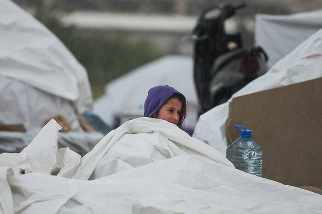 이스라엘군이 친이란 무장정파 헤즈볼라를 겨냥해 21일 새벽 레바논 수도 베이루트에 대규모 공습을 감행한 가운데, 한 피란민이 비를 피하기 위해 방수포로 임시 거처를 만들어 들어가 있다. 로이터 연합뉴스
