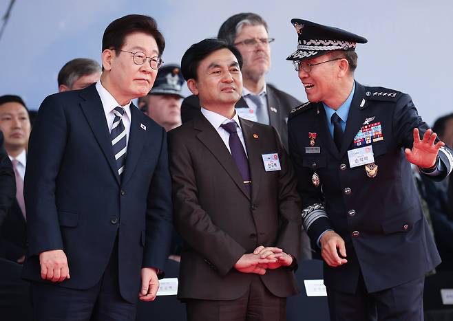 President Lee Jae Myung listens to an explanation from Air Force Chief of Staff Lt. Gen. Son Seok-rak during the rollout ceremony for the KF-21 fighter jet at Korea Aerospace Industries in Sacheon, South Gyeongsang Province, Wednesday. Defense Minister Ahn Gyu-back is in the center. (Pool Photo via Yonhap)