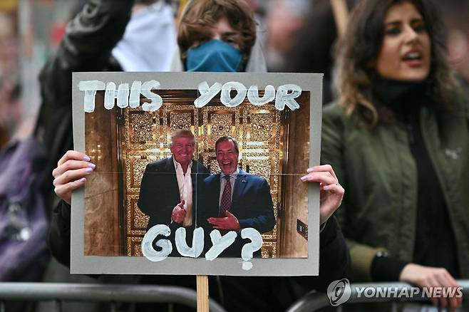 선거 유세장 앞의 영국개혁당 반대 시위대가 트럼프 대통령과 패라지 대표가 함께 찍은 사진을 들고 있다 [AFP 연합뉴스 자료사진. 재판매 및 DB 금지]