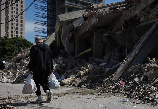 28일 레바논 베이루트에서 한 남자가 구호품과 식량이 담긴 가방을 들고 공습 현장을 지나가고 있다. /연합뉴스