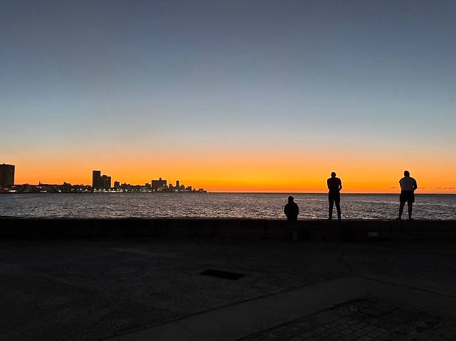 지난 23일 쿠바 아바나 말레콘 해안의 노을을 배경으로 쿠바인들이 낚시를 하고 있다. 10년 만에 찾은 쿠바 말레콘의 거센 파도는 여전했지만, 쿠바인들이 마주한 삶은 더 거칠어져 있었다. /박국희 특파원