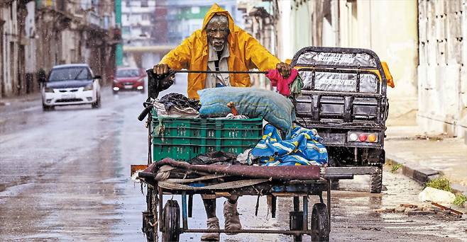 우비를 걸친 노인이 쿠바 수도 아바나 거리를 손수레를 밀며 지나고 있다. 미국이 최근 베네수엘라산 원유 공급을 차단하면서, 쿠바 전역에서 대규모 정전 사태가 벌어지고 국민들이 에너지난에 시달리고 있다. /AFP 연합뉴스