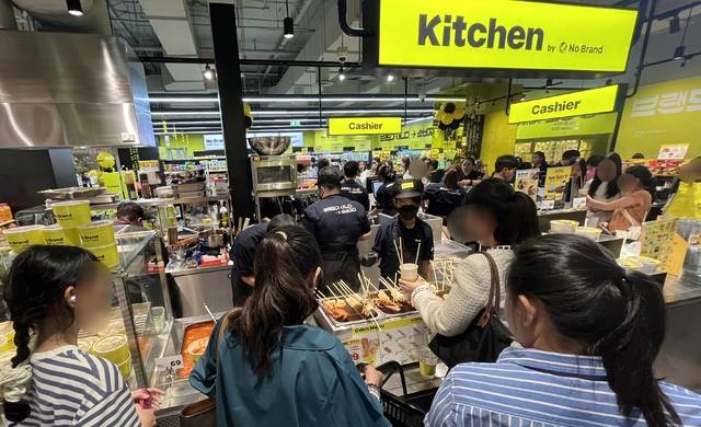 이마트가 방콕의 랜드마크 쇼핑몰 ‘센트럴 방나’에 오픈한 노브랜드 1호점 내에 위치한 한국 키친 코너에 태국 고객들이 주문한 음식을 받아들고 있다.(이마트 제공)