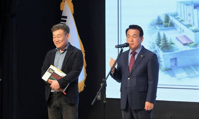 지난 3월 31일 열린 논산시 복합문화체육센터 ‘온담’ 개관식 현장에서 기념사를 이어가던 백성현 논산시장이 논산시 도시재생과 공공건축팀 김영일 팀장(왼쪽)을 무대 위로 직접 불러 시민들 앞에서 그간의 노고를 치하하며 공개 칭찬을 하고 있다.(사진=논산시 제공)