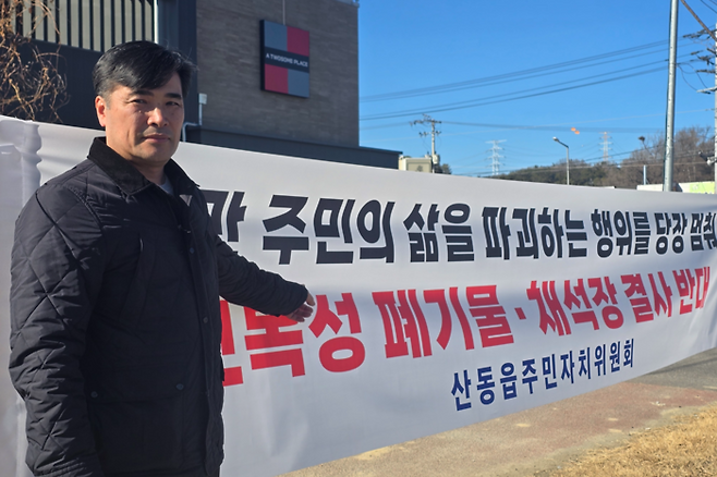 최광재 산동읍단체장협의회장이 주민들이 내건 현수막 앞에서 산동읍 일대에 추진 중인 지정산업폐기물처리시설과 초대형 채석장 반대 이유를 설명하고 있다. 박용기기자