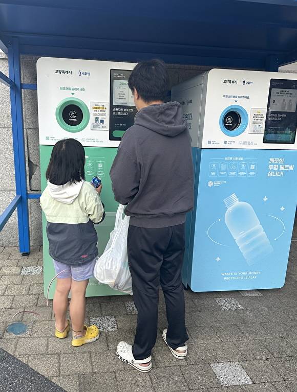 인공지능(AI) 기반 재활용품 무인회수기 앞에서 한 시민이 아이와 함께 투명 페트병을 직접 배출하며 현금으로 환전 가능한 포인트를 적립하고 있다. [사진=고양시]
