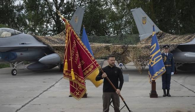 볼로디미르 젤렌스키 우크라이나 대통령이 2024년 8월 서방으로부터 제공받은 F-16 전투기를 배경으로 깃발을 들고 있다. AP 연합뉴스