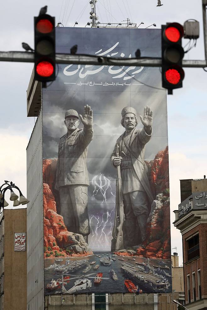 지난 13일 이란 테헤란에 ‘이란 역사 영웅들을 기리며’란 문구와 함께 두 인물이 미국 항공모함 등을 막는 듯한 그림이 걸려 있다. 왼쪽은 지난달 26일 호르무즈해협 봉쇄 작전 중 이스라엘 공습에 숨진 알리레자 탕시리 이슬람혁명수비대 해군 사령관이다. 오른쪽은 1915년 영국군과 싸우다 사망한 민족 영웅 라이스 알리 델바리. 로이터=연합뉴스