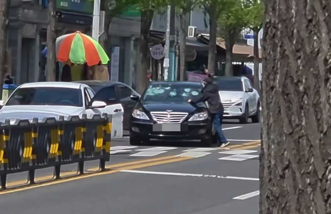 15일 오전 11시 16분께 울산 중구 다운동의 한 도로 위에서 50대 남성 A 씨가 검은색 승용차를 몸으로 막은 뒤 손에 든 고무망치로 차량 앞유리를 수차례 휘두르는 장면이 인근 주민들에게 촬영됐다. 독자 제공