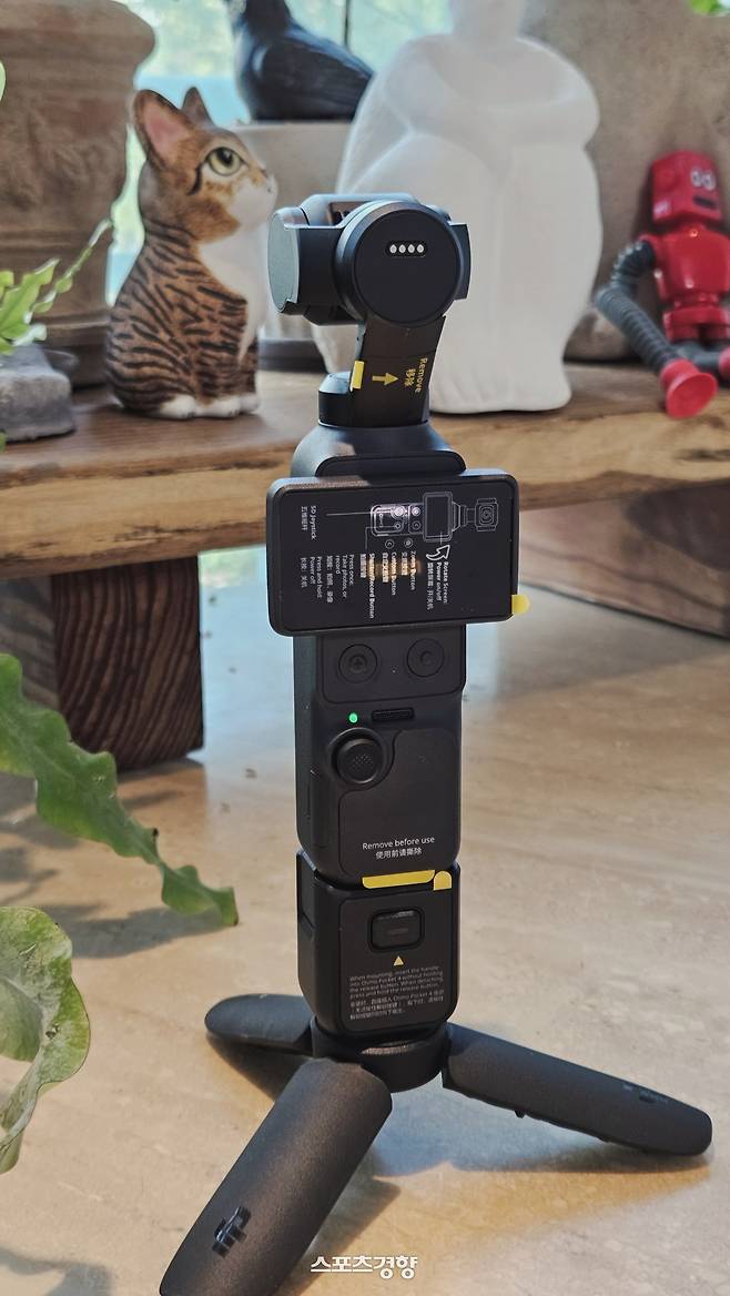 오즈모 포켓4 본체와 USB C포트 연결부, 하체 삼각대를 결합한 외형이다. 카메라 헤드 뒷편에 외부 액세서리를 더할 수 있는 결착형 4핀 접합 단자가 보이고 있다.  이렇게 장착하면 카메라 헤드(머리)에서 하단부 다리 밑면까지 22cm 세로 길이가 나온다. 사진 | 손재철기자