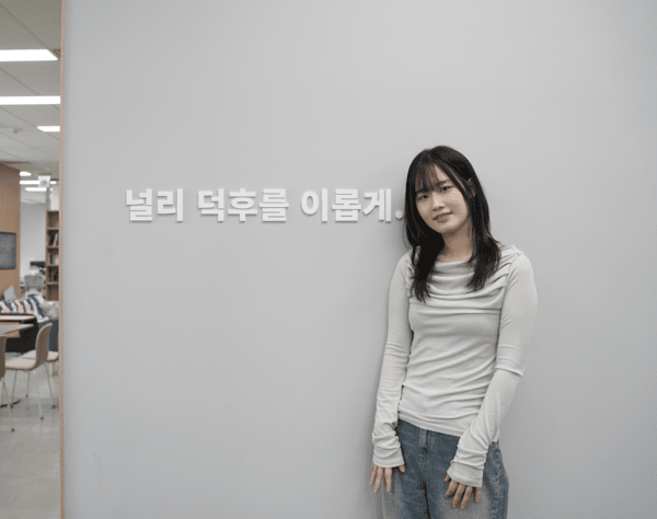 라프텔 사무실 벽에 적힌 "널리 덕후를 이롭게." 문구 앞에 선 김수민 라프텔 마케팅팀 매니저. 사진=ER 이코노믹리뷰 김연제 기자.