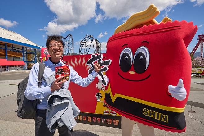 16일 오전 일본 야마나시현 후지요시다시에 위치한 놀이공원 후지큐 하이랜드(하이랜드)에 등장한 농심 ‘신(SHIN)’ 캐릭터와 함께 방문객이 신라면을 들고 즐거워 하고 있다.(사진제공 농심)